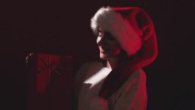 A woman in a warm new years dress in a red santa hat on festive background holds a red gift box with a bow. - Powered by Shutterstock - Get 15% off with code: PIKWIZARD15