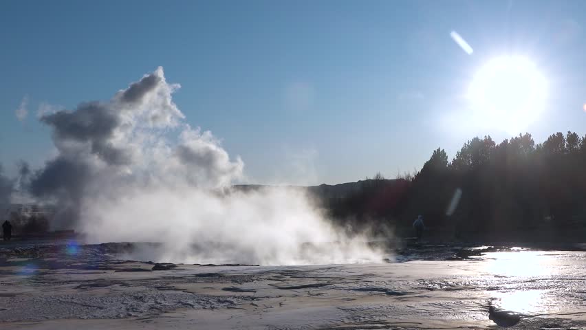 Witness the powerful eruption of a geyser at the Geysir geothermal area in Iceland, surrounded by stunning landscapes under a clear blue sky.