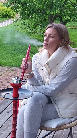Woman smokes hookah on in backyard. Outdoor recreation with friends Vertical video. Taken from hand. High quality 4k footage