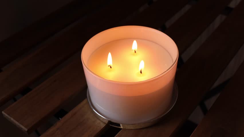 A candle with three wicks burns on a table. Soft light brings a cozy home atmosphere. Candles are part of traditions for comfort, especially during the holidays. navidad
