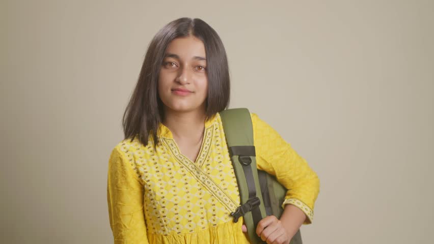 Carrying a backpack on her shoulder by a South Asian teenage girl dressed in a traditional yellow outfit