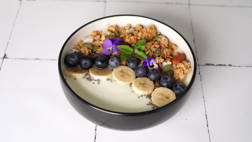 Woman hands rotates a plate with a granola, yogurt, berries and flowers