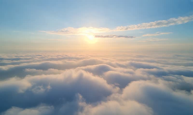 flying shot over the clouds in day going towards the sun
