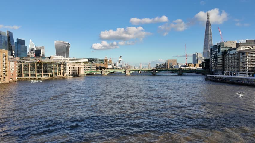 Wide view of the River Thames with London modern skyline, including the Shard and iconic architecture, under a clear blue sky.