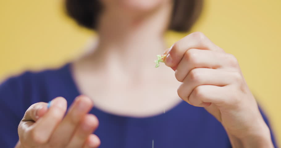 Close-up of woman opening a capsule pill in focus against a yellow background