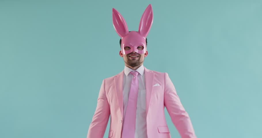 A man is joyfully celebrating in a vibrant pink bunny costume, full of energy, against a bright teal background