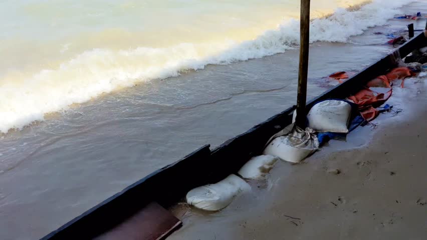 Waves of sea water that is hitting the wood board and the sack filled with sand at the seashore