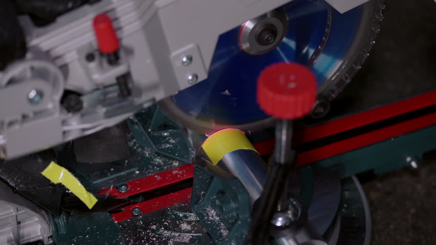 Sawing an aluminum part with a chop saw. Side view of the fast spinning blade used for machining round metal material. Industrial work in a dark outdoor environment. Dust and chips flying around.