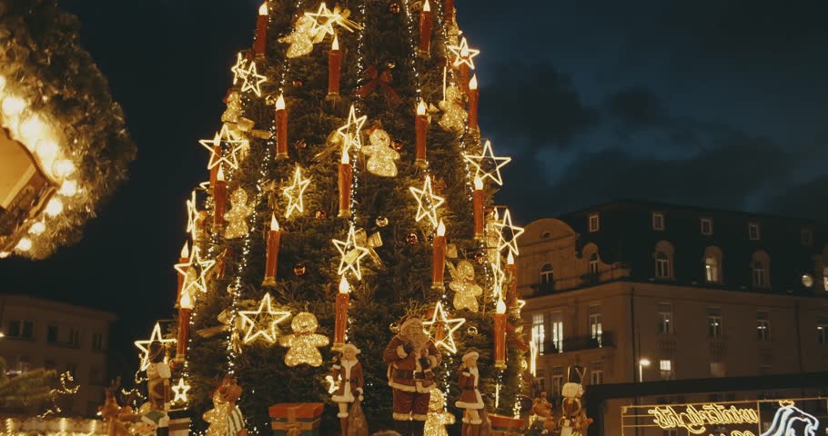 Christmas tree decorated with garlands stars glows at night. main Christmas tree top on background of dark sky. celebrations at fair in Europe. Christmas houses shops stalls entertainment illumination