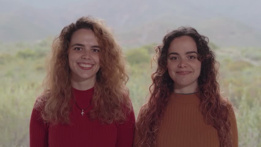 Beautiful Twin Sisters Laughing Out Loud in the Green Nature with Mountains in the Background. Hermosas Hermanas Gemelas Riendo a Carcajadas en la Verde Naturaleza con Montañas de Fondo
