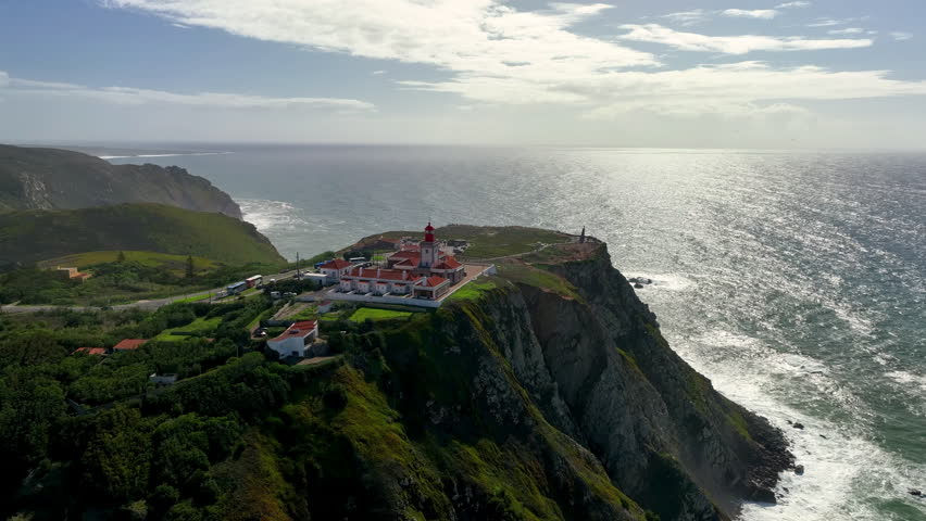 4k aerial view of dangerous cliff and Cape Roca lighthouse Cabo da Roca red and white lighthouse at Europe western edge. Portugal