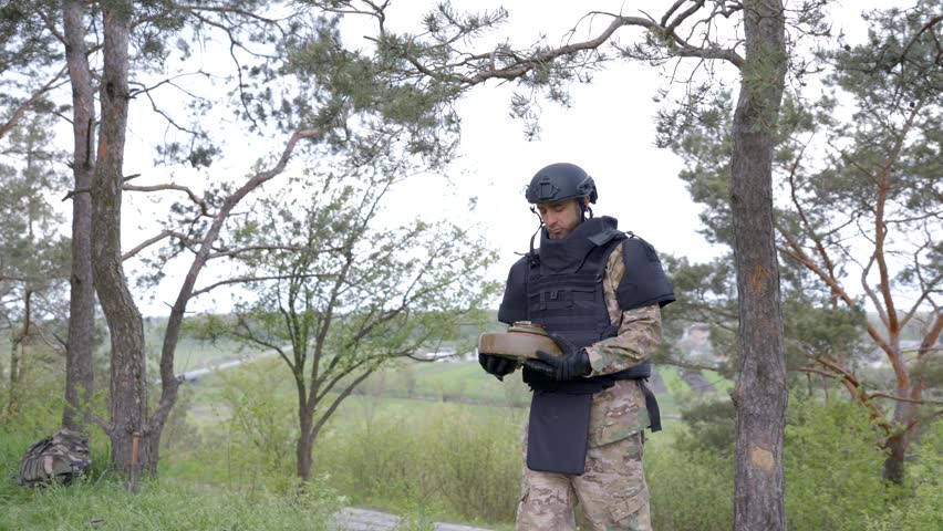 A man in a special suit works with a detector and found an explosive device. A man tries to neutralize an anti-tank mine