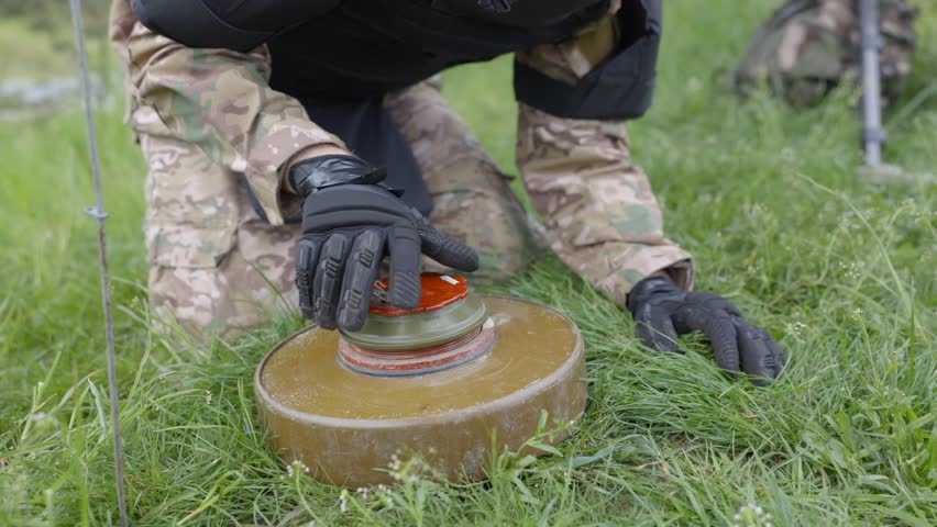 A man in a special suit works with a detector and found an explosive device. A man tries to neutralize an anti-tank mine