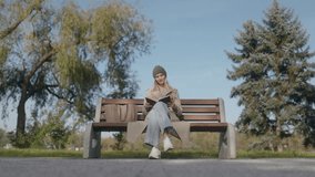 Dressed for the season, a woman reads on a bench in the park, enjoying a peaceful escape in nature. Her beige coat and knit hat add warmth to the serene autumn atmosphere. - Powered by Shutterstock - Get 15% off with code: PIKWIZARD15