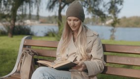 A woman with a joyful expression reads a book on a park bench, surrounded by autumn colors. Her cozy outfit and the sunny day create a serene, relaxing atmosphere. - Powered by Shutterstock - Get 15% off with code: PIKWIZARD15