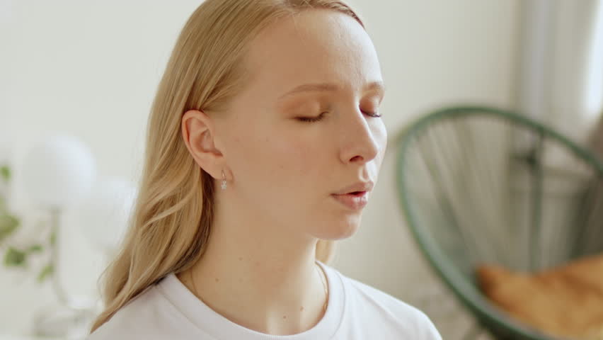 Relaxed calm woman with closed eyes doing breathing meditating practices at home. Making deep breath-exhalation pranayama exercises.