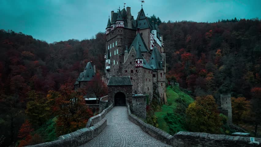 Girl in red hooded cloak walks on cobblestone path on autumn evening to ancient castle of Eltz, Rhineland-Palatinate, Germany. High quality 4k footage