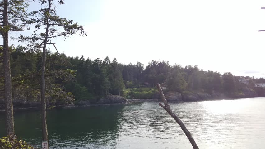 Panning right across Neck Point Park in Nanaimo, BC, Canada, on a clear day. The serene coastal scene features rocky islands, calm ocean waters, and a cloudy sky, with distant mountains on the horizon