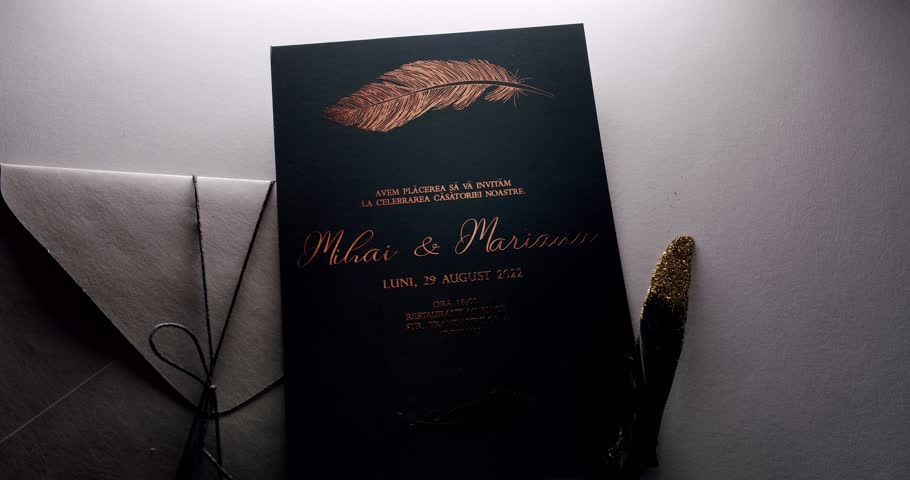 Elegant wedding invitation card featuring a gold feather design and matching envelope. The invitation displays refined calligraphy and a sophisticated layout, perfect for announcing a special event.