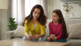 Happy family loving Caucasian woman mother female mom counting dollars cash dollar bill saving giving little girl child kid daughter allowance pocket money financial literacy income budget inside home - Powered by Shutterstock - Get 15% off with code: PIKWIZARD15