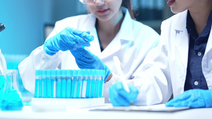 Two scientists in lab coats are analyzing test tubes containing blue liquid and taking notes