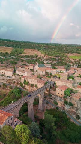 Aerial view of the medieval village of Minerve in the south of France. Historic stone buildings, a beautiful arched bridge, and a colorful rainbow in the sky.