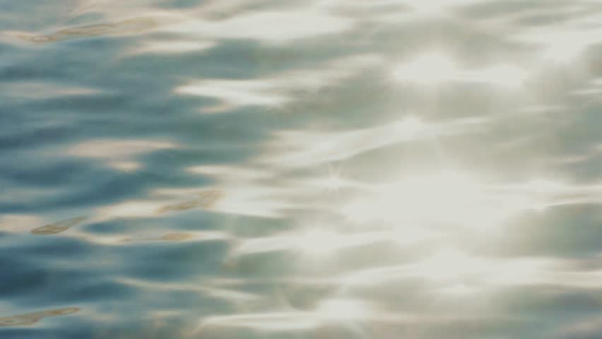 The bright sunlight creates mesmerizing reflections on the surface of the water. Gentle waves ripple, enhancing the shimmering patterns in this tranquil setting on a sunny day.