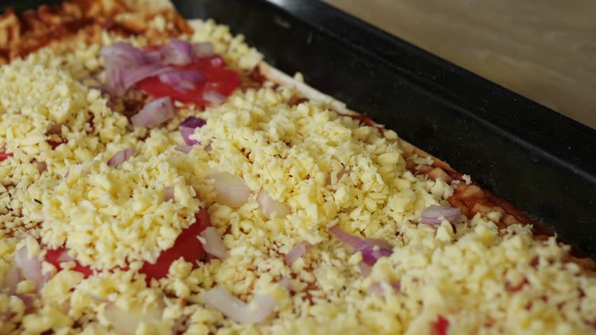 Preparing a delicious homemade pizza with fresh tomato slices, onions, and cheese toppings in the metal food tray, closeup shot.