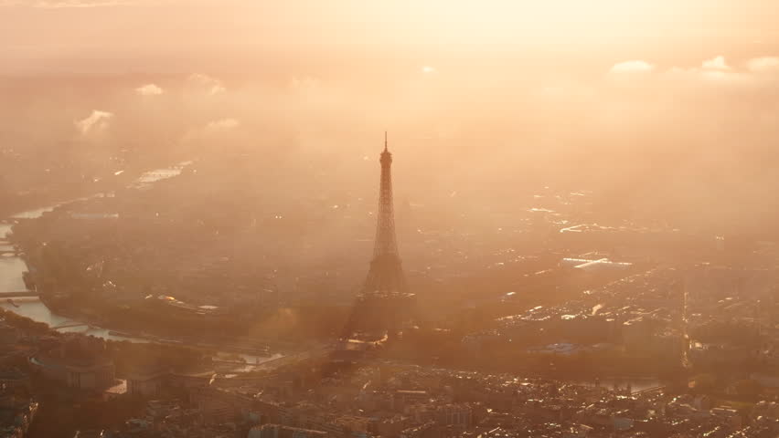 Circling aerial shot of the Eiffel tower backlit by the sunrise