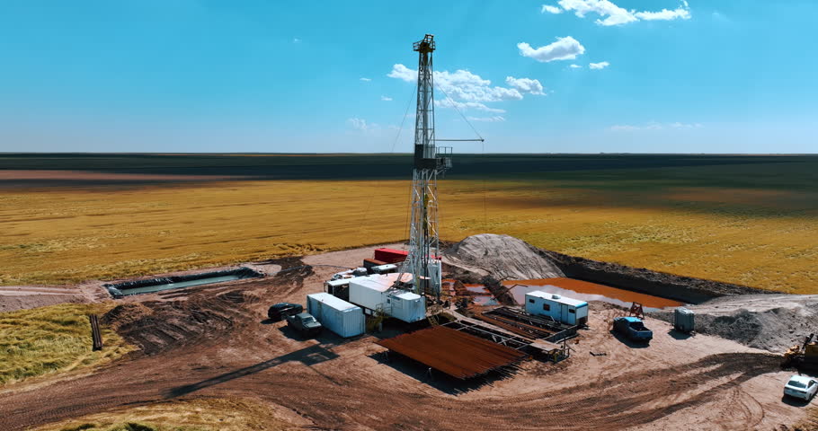White metal derrick in the center of drilling site. Industrial production of oil or gas in the deserted area.