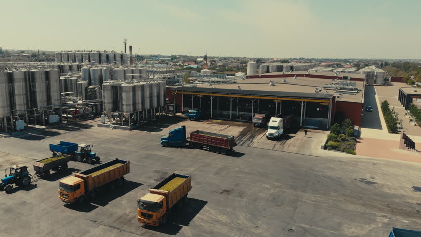 Multiple transportation trucks driving at the industrial factory. Industrial factory deals with the manufacturing of alcoholic wine drinks. Industrial storage tanks near production factory