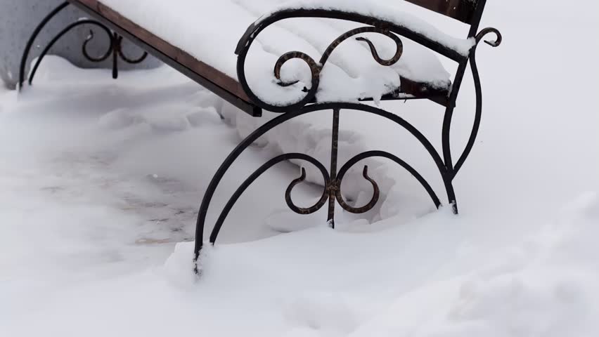 A bench in a park under a layer of snow in winter nature. Slow motion