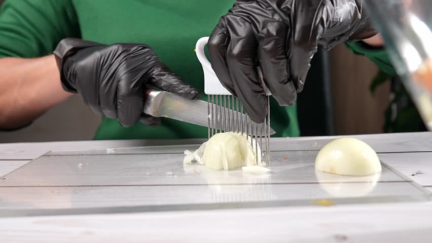 Chef wearing black gloves is slicing an onion for olivier salad using a knife and a special slicer