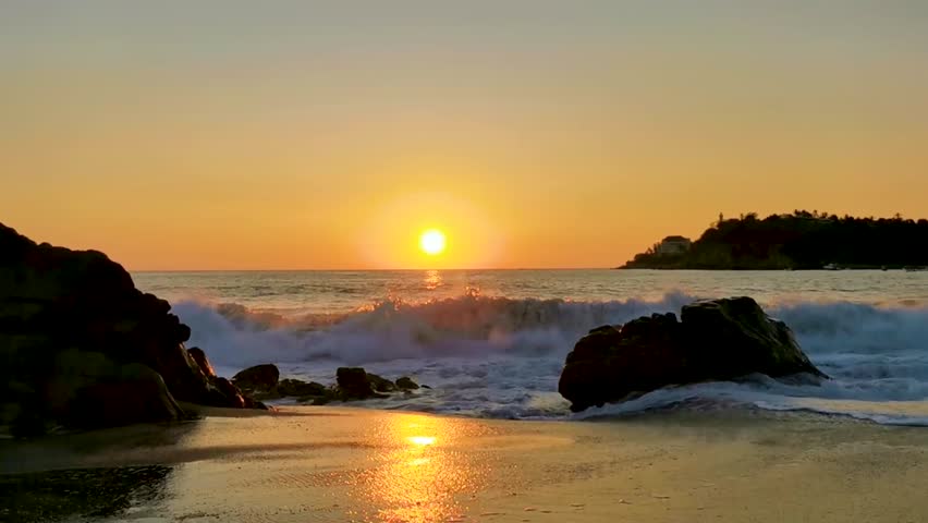 Beautiful stunning colorful and golden sunset in yellow orange red on beach and big huge surfer wave and rocks cliff panorama in tropical nature in Zicatela Puerto Escondido Oaxaca Mexico.