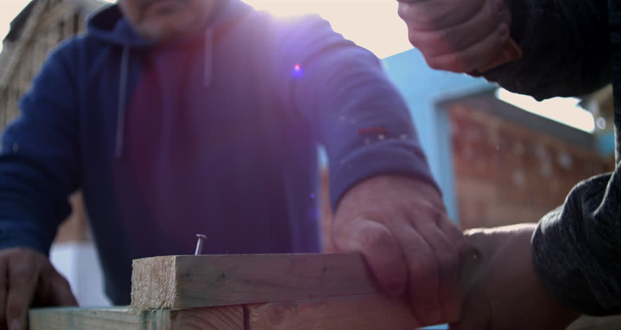 Two men hammering nail into wood, securing plank with teamwork, close-up of intense carpentry work, construction precision in slow motion at 800 fps