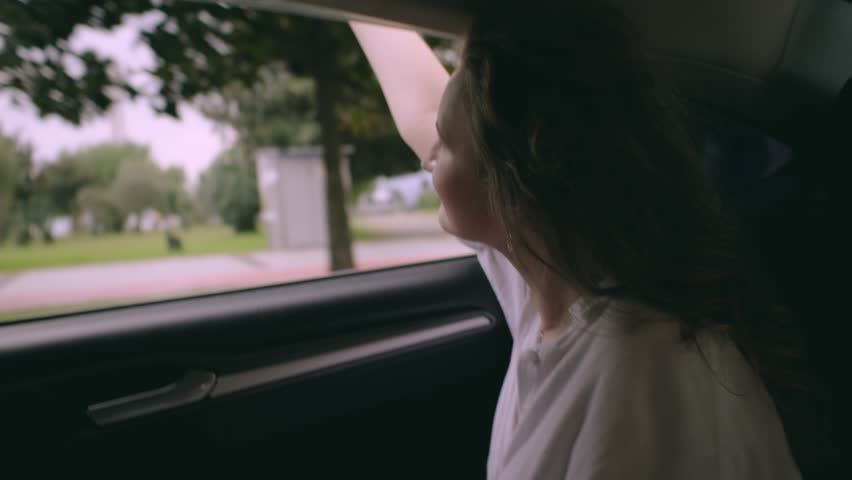 Beautiful young Girl lookinh in the Window Enjoying Wind Daytime in a good car