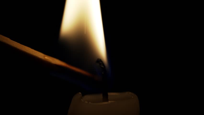 A match is struck to ignite the flame of a candle in a dimly lit room. The soft glow from the candle begins to illuminate the surroundings, creating a warm ambiance.