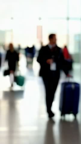 Blurred image of a busy airport terminal with travelers walking and carrying bags, creating a dynamic and bustling atmosphere.