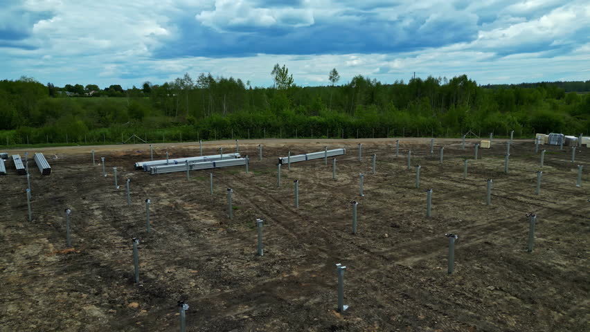 Aerial low orbit of an expansive solar farm site under construction, featuring aligned solar panels scaffolding beams in empty field