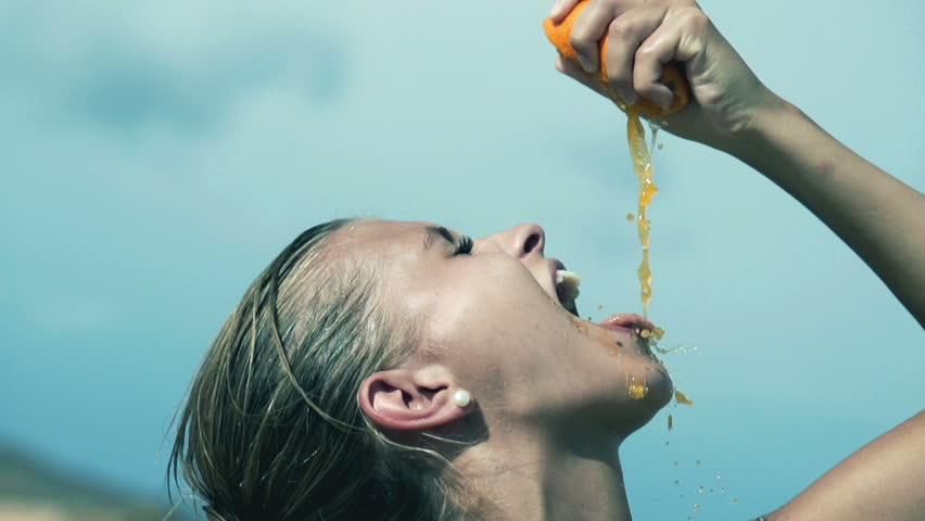 Young woman squeezing orange into the mouth, slow motion shot at 240fps
