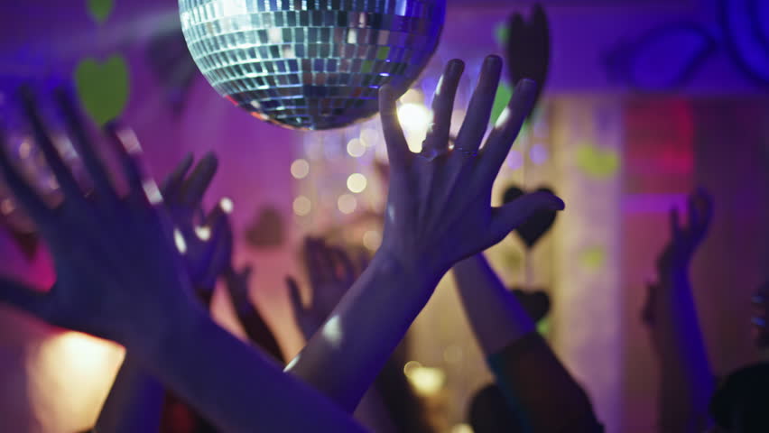 Clubbing people hands dancing in neon light nightclub closeup. Energetic arms reach to disco ball in dance club atmosphere. Festive mood captivating youthful clubbers crowd on lively dancefloor. 