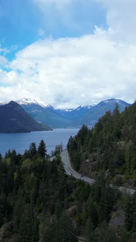 Aerial view of cars driving on a scenic road by a lake with mountains in the background. British Columbia, Canada.