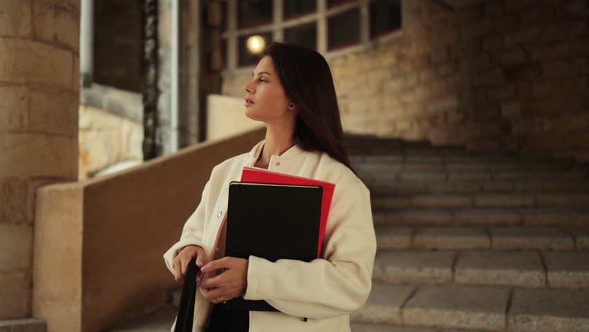 Attractive girl, model, posing near the stone, university stairs with notebooks in her hands, close portrait of a confident, successful student, education, lessons, academic year, faculty, fashion