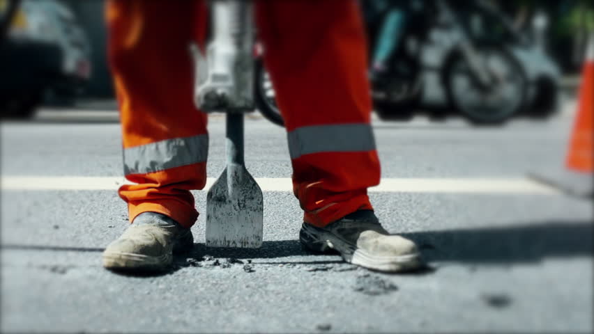 Worker operating a jackhammer on the street, breaking up asphalt during roadwork, showcasing a labor-intensive job in an urban environment