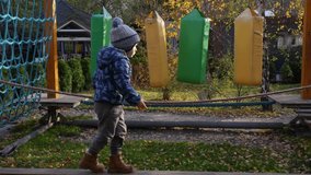 Child in blue jacket and boots enjoying obstacle course on playground on sunny autumn day. Concept of active play, childhood adventure, and outdoor activities. High quality 4k footage - Powered by Shutterstock - Get 15% off with code: PIKWIZARD15