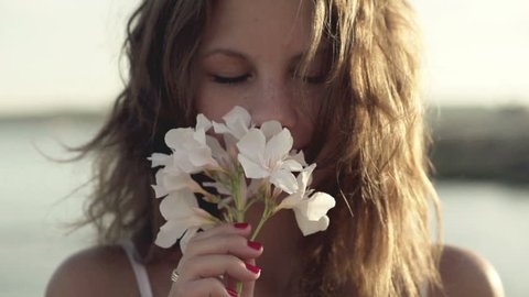 Young woman standing on seashore and smelling flower, slow motion shot at 120fps
