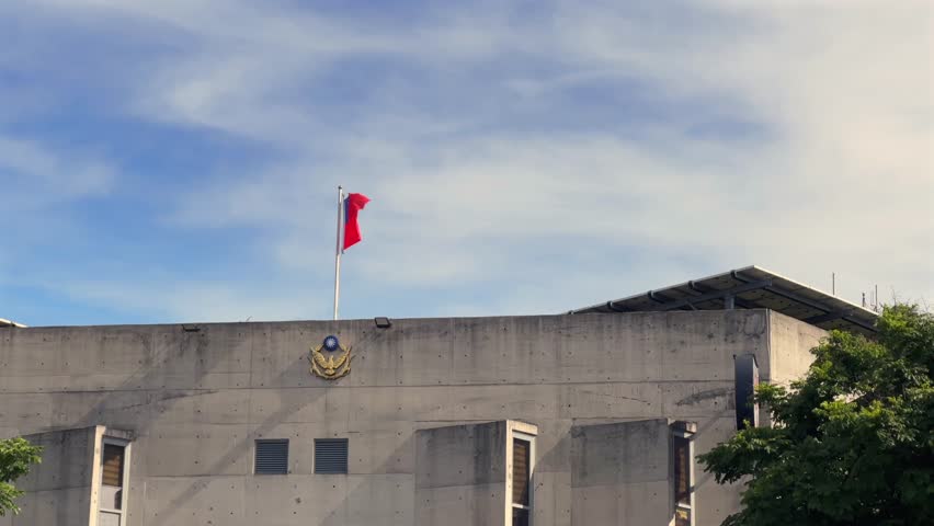 The Taiwan flag waving high atop a modern building against a clear blue sky, symbolizing pride, freedom, and national identity.