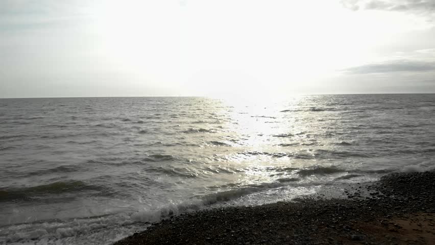 Slow motion shot over ocean waves, flying toward the bright sun on the horizon at sunset