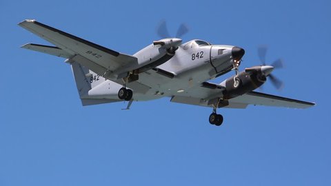 Small grey airplane with propeller engines flying high in clear blue sky