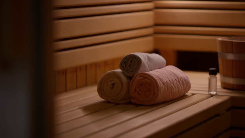 Cozy interior of a wooden sauna with neatly rolled towels, a wooden bucket, and a small essential oil bottle, creating a tranquil and relaxing ambiance. Concept of wellness and self-care